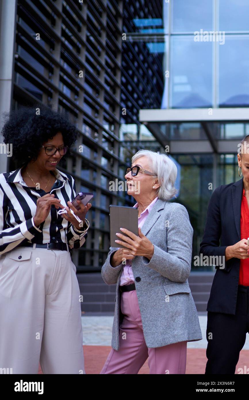 Verticale. Team di donne aziendali multiculturali in vestibilità formale che utilizzano e guardano il cellulare Foto Stock