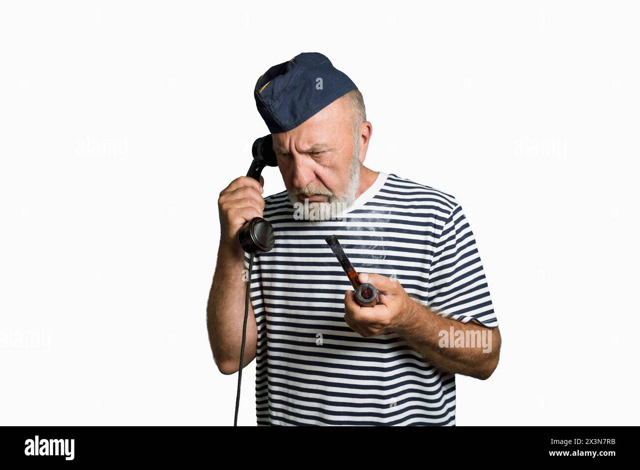 Un vecchio marinaio del passato sta parlando al telefono. Verticale su sfondo bianco. Sailor con un tubo fumante e un vecchio telefono in mano Foto Stock