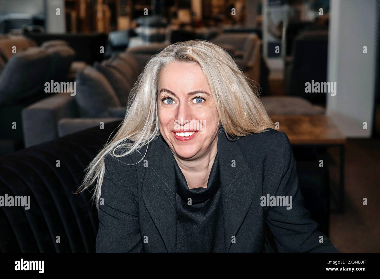 Donna matura e radiosa con capelli argentati, che trasuda carisma in un formale ensemble nero, deliziandosi con un'esposizione di mobili di lusso Foto Stock