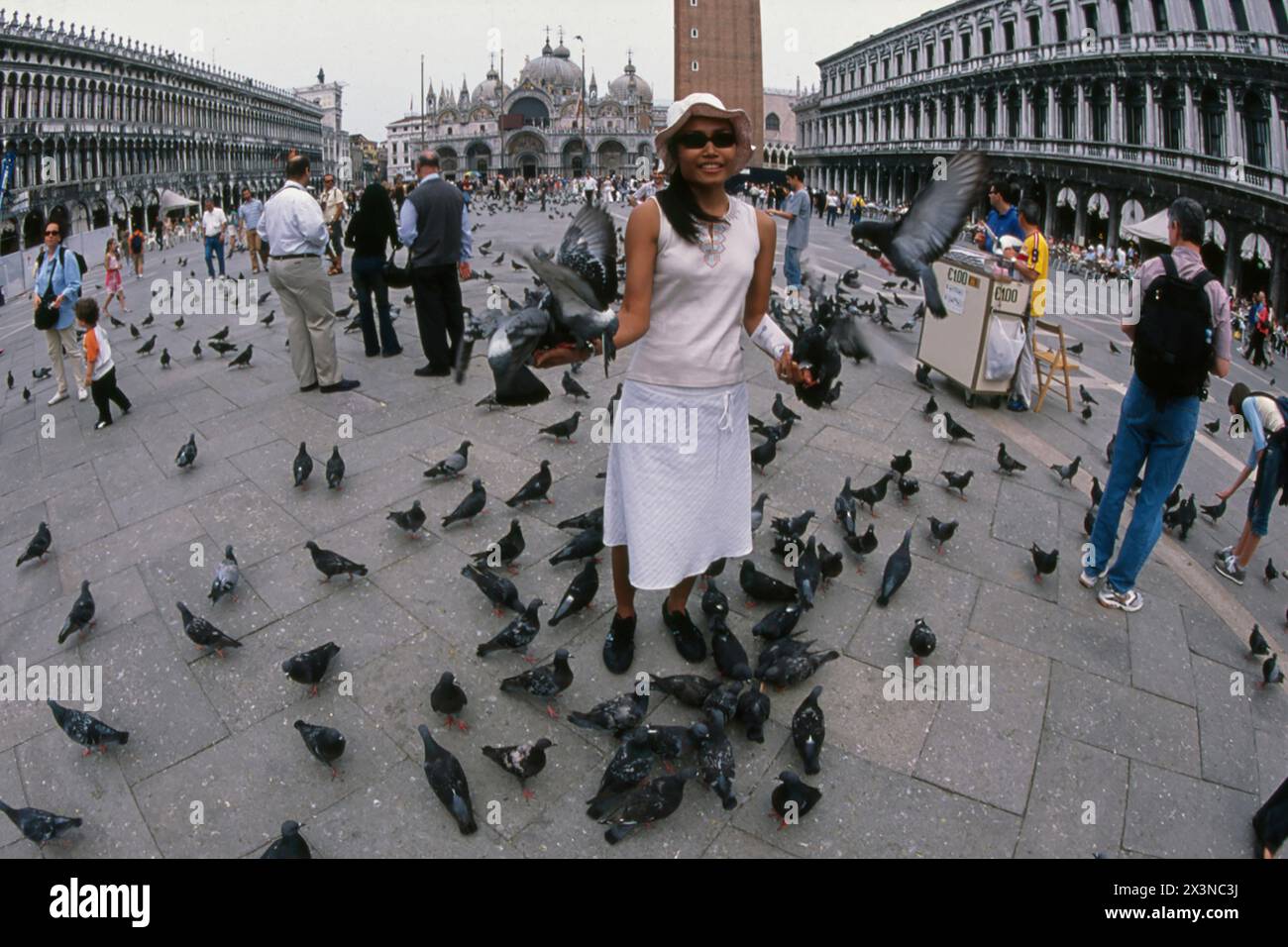 Donna che dà da mangiare ai piccioni con la basilica di San Marco sullo sfondo, Piazza San Marco, Venezia, Italia Foto Stock