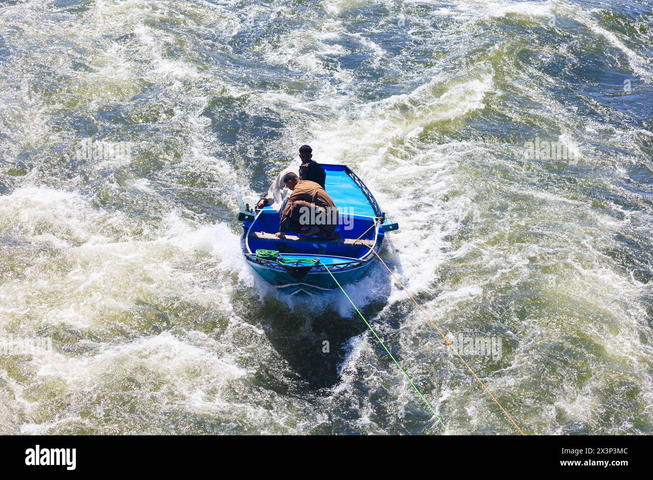 Due uomini egiziani su una barca a remi, che prendono un rimorchio da una nave da crociera turistica del Nilo di passaggio. Fiume Nilo, Egitto Foto Stock