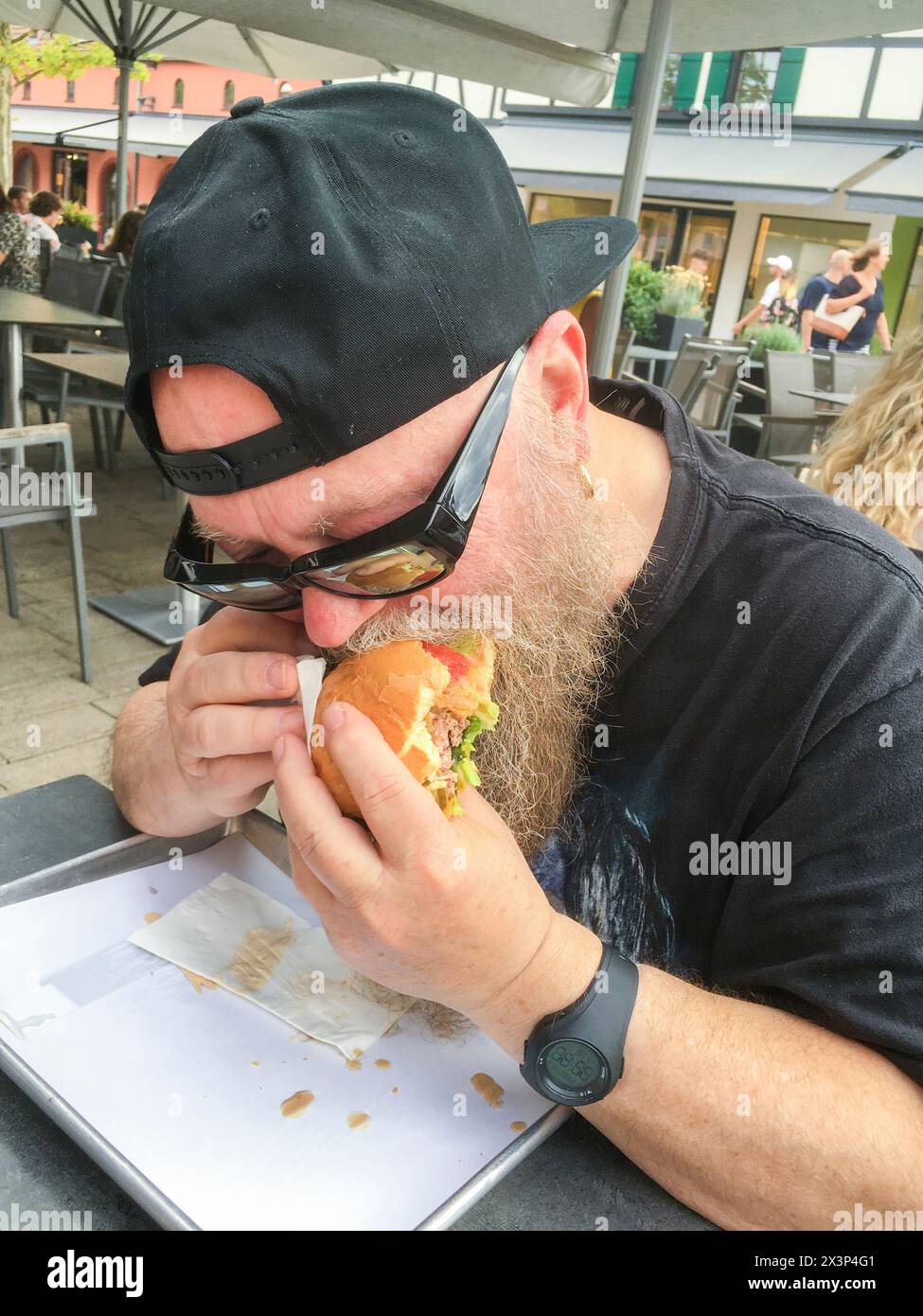 Mann mit langem Bart beißt genüßlich in einen Burger Foto Stock