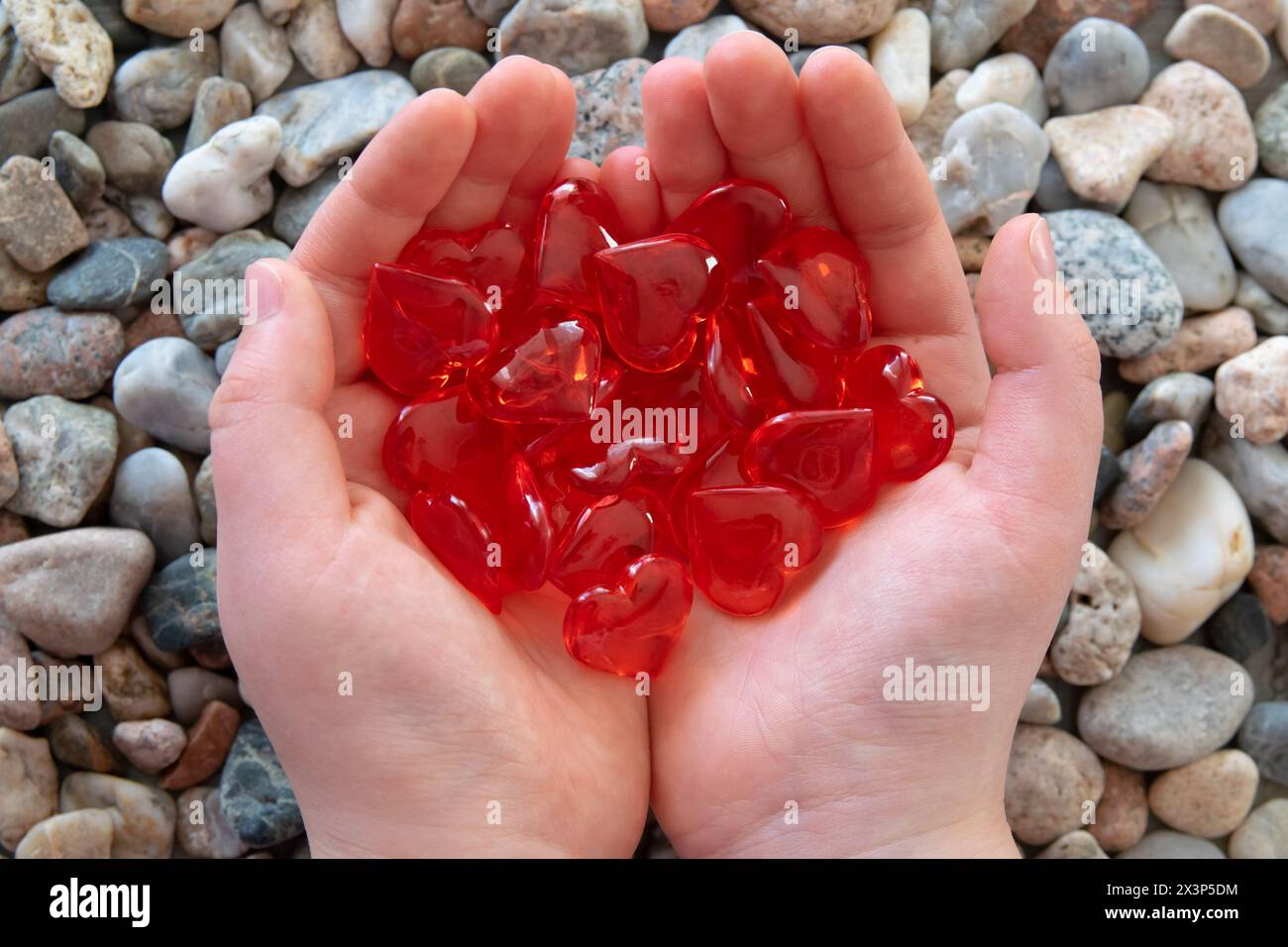 Cuori di vetro rosso brillante nelle mani dei bambini sullo sfondo delle pietre. Concetto di San Valentino e amore romantico. Foto Stock
