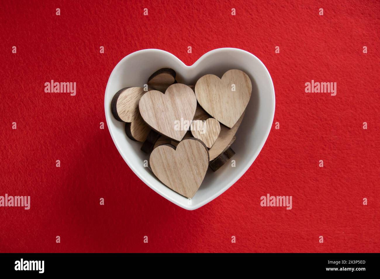 Molti cuori di legno nel piatto su sfondo rosso con spazio immacolato. Concetto di San Valentino e amore romantico. Foto Stock