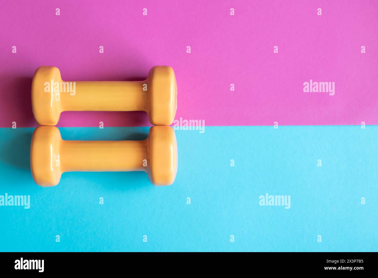 Due manubri arancioni su sfondo rosa e blu con spazio per le copie. Uno strumento per l'allenamento, lo sport e l'attività in estate. Foto Stock
