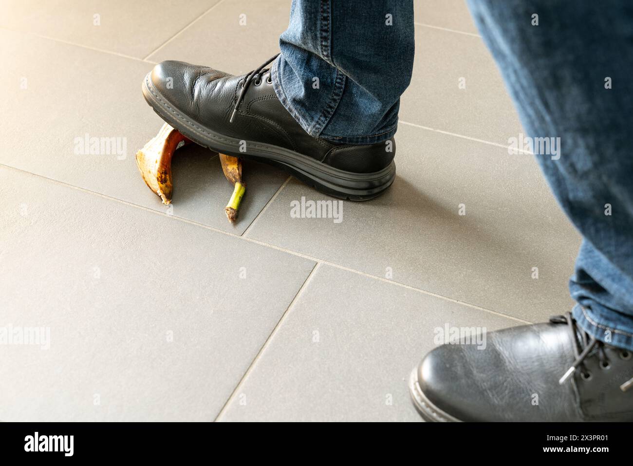 Primo piano di un uomo con scarpe nere che si accostano a una buccia di banana mentre cammina. Concetto di pericolo di inciampare o cadere. Solo piedi visibili. Foto Stock