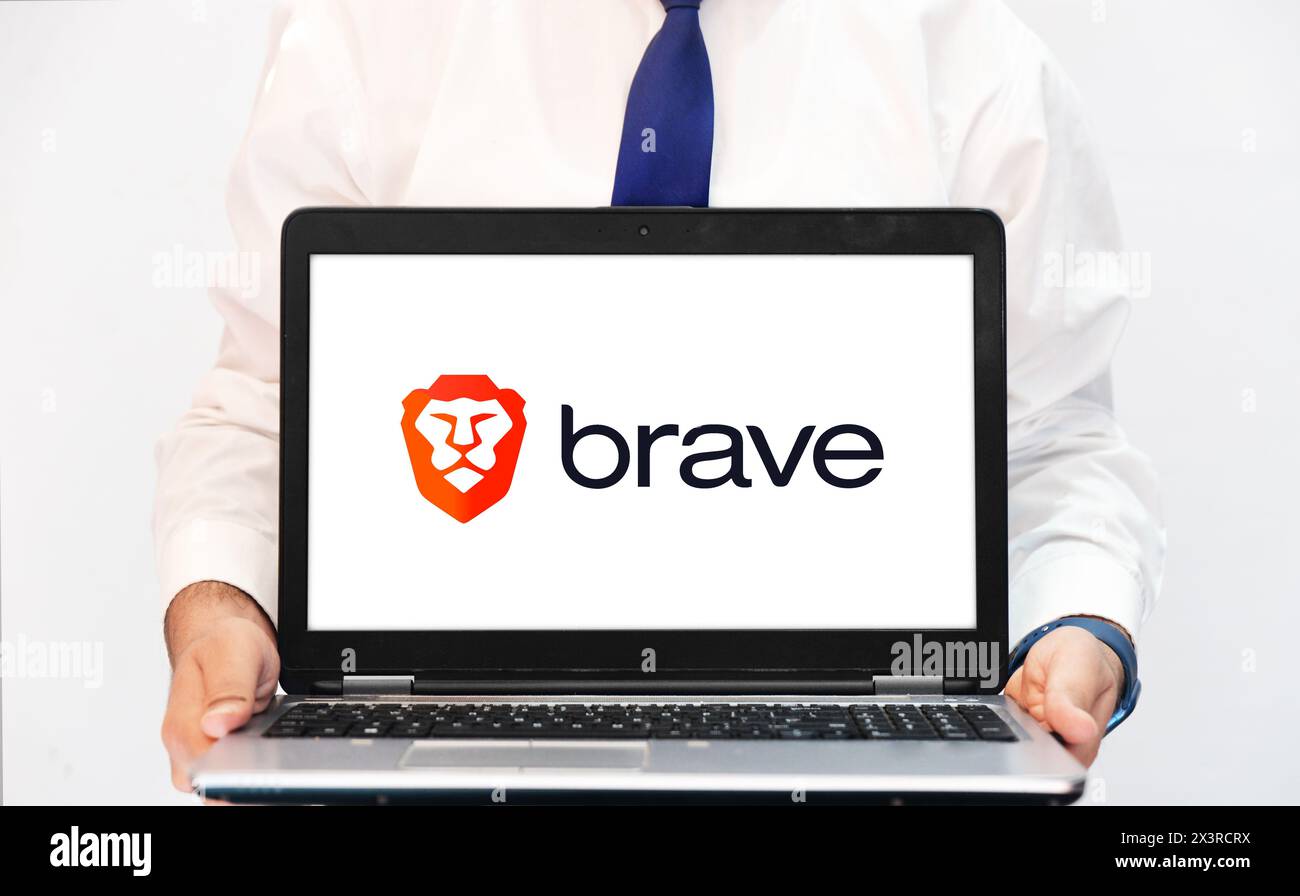 Brave Browser sullo schermo del notebook con una persona che tiene aperto il laptop, editoriale. Moderno browser a forma di leone chiamato Brave, sfondo Foto Stock