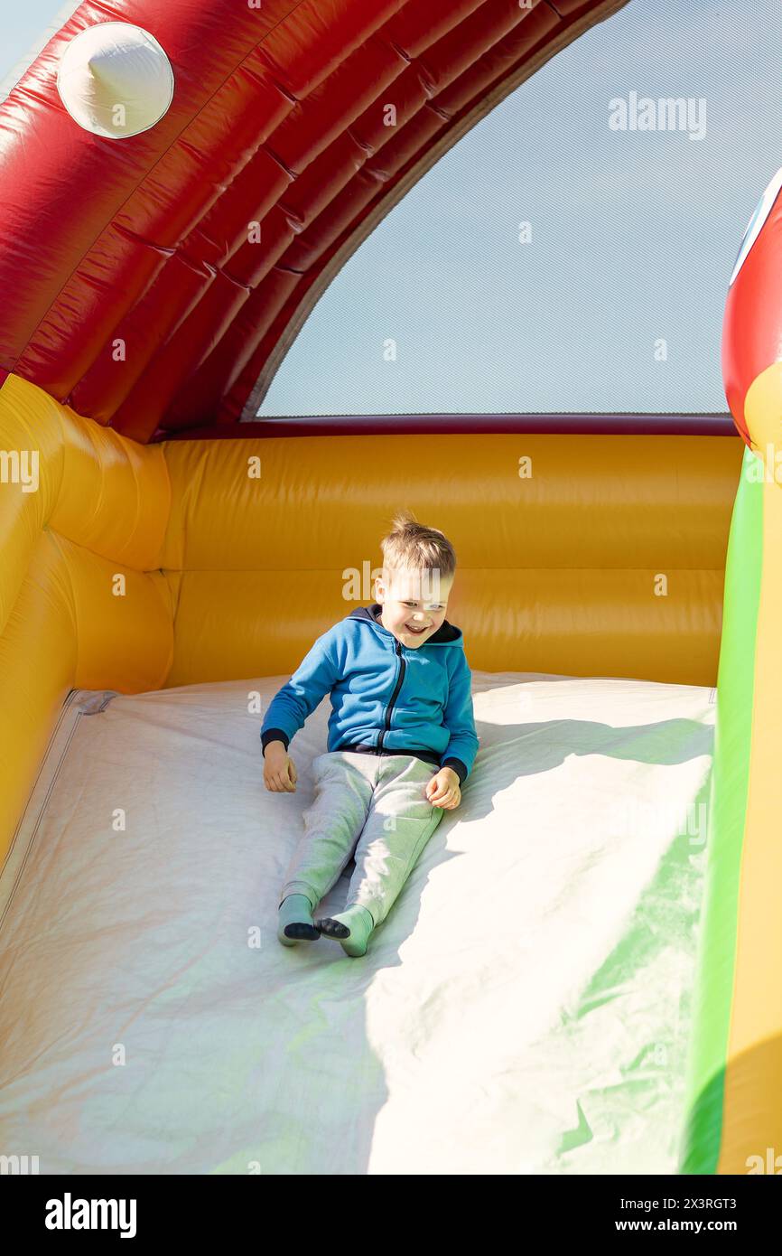 Un bambino piccolo cavalca su uno scivolo gonfiabile multicolore. Foto Stock