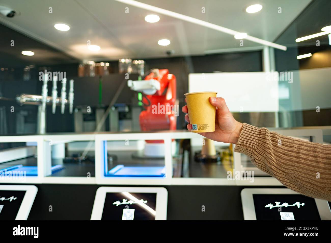 Tazza di caffè di carta in mano maschile, il robot Tesla prepara il caffè, l'affascinante Tesla Bot dimostra agilità, prepara abilmente la qualità del barista, Berlino, Ger Foto Stock