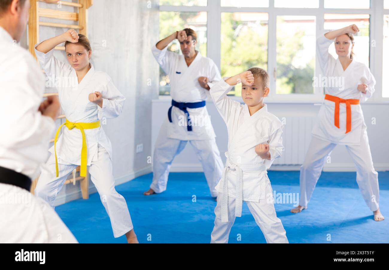 Ragazzo in kimono con la sua famiglia all'allenamento di gruppo in palestra pratica karate punch block tecnica Foto Stock
