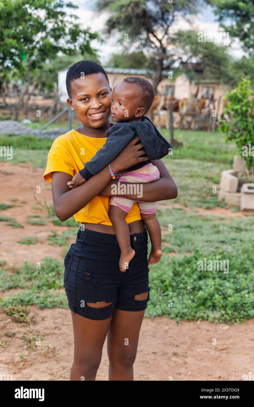 villaggio africano , famiglia africana giovane madre e bambino in piedi davanti alla casa, madre che tiene il bambino Foto Stock