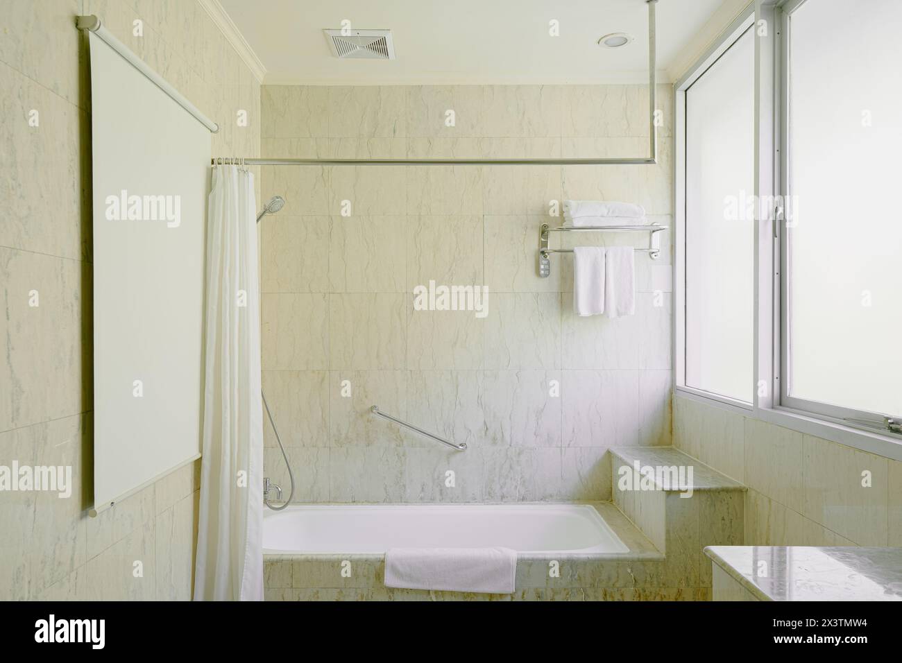 Bagno di lusso con vasca e vasca a zampa d'artiglio sotto una finestra circondata da pavimento e pareti in piastrelle di marmo Foto Stock