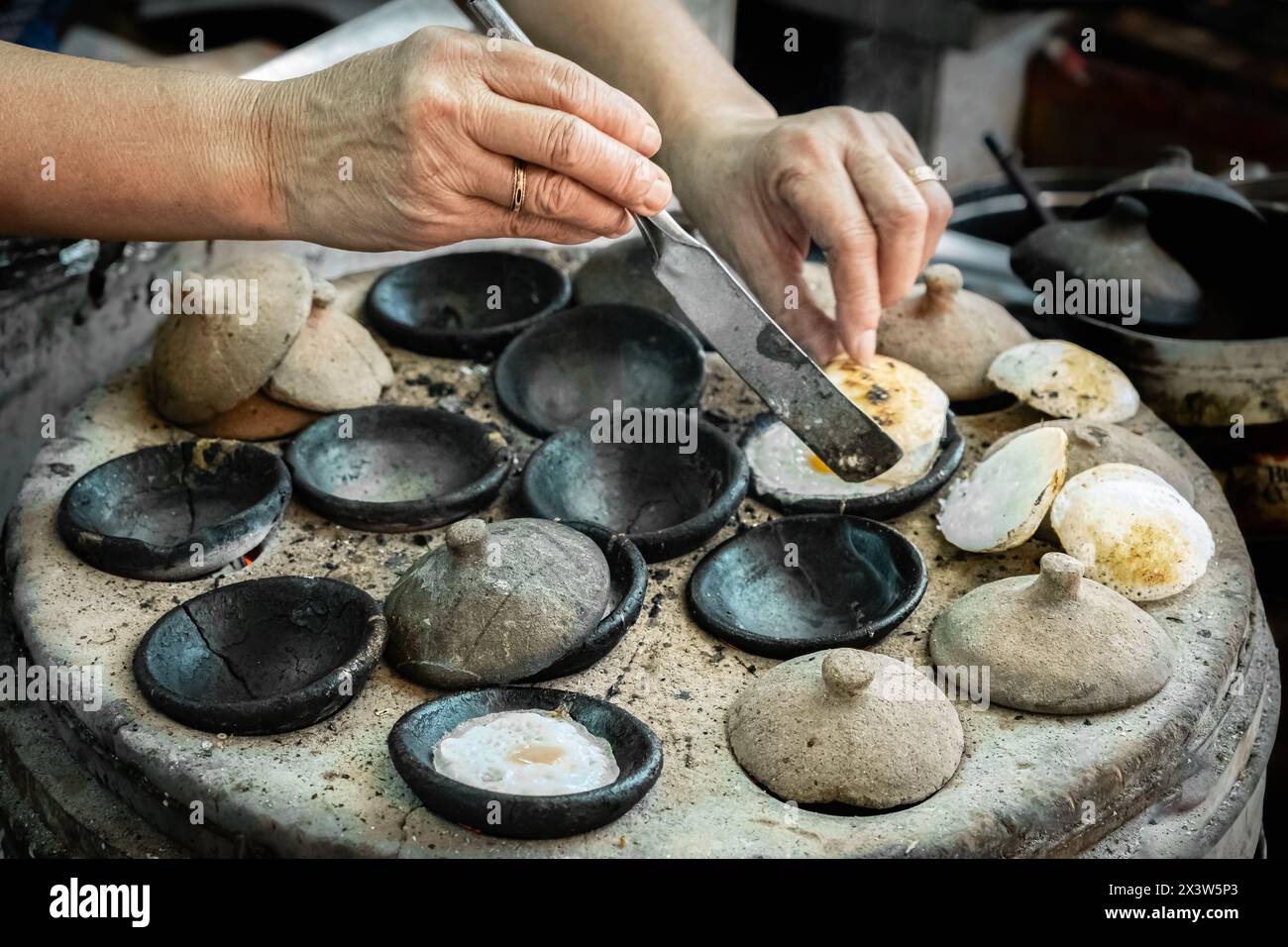 Mini uova fritte vietnamite, con farina di riso, cucinare per strada. Donna asiatica che prepara la tradizionale colazione vietnamita. Il banh CAN è un piatto popolare Foto Stock