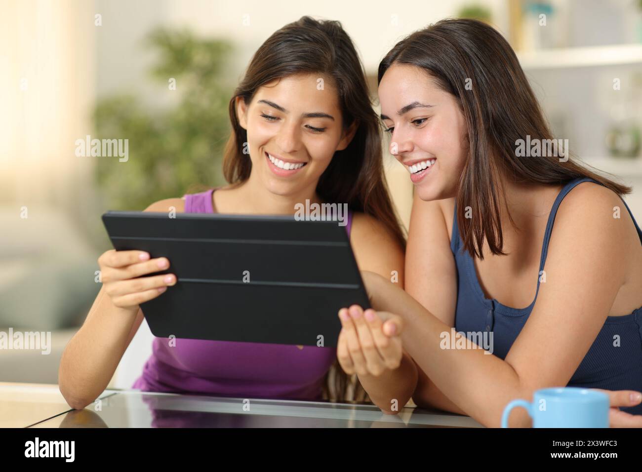 Due donne felici che guardano i contenuti multimediali su un tablet a casa Foto Stock