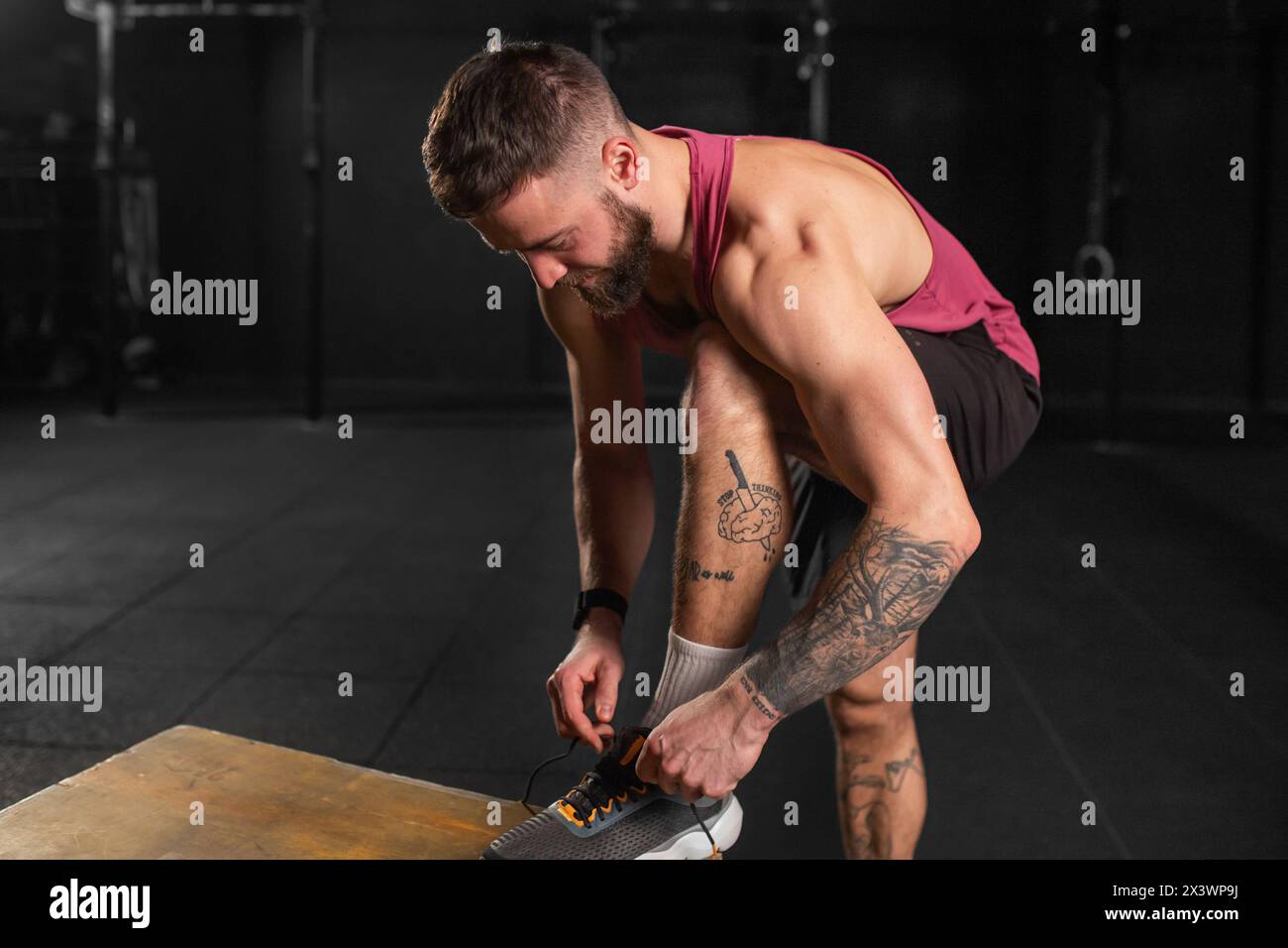 Bell'uomo muscoloso che lega lacci alle scarpe da ginnastica in palestra. Allenamento di routine per la salute fisica e mentale. Foto Stock
