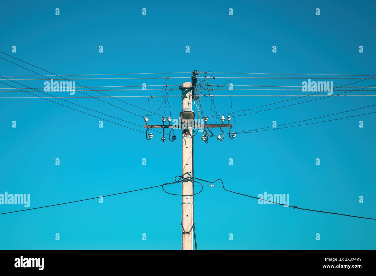 Palo elettrico con cavi sospesi e lampada per illuminazione stradale contro il cielo blu Foto Stock