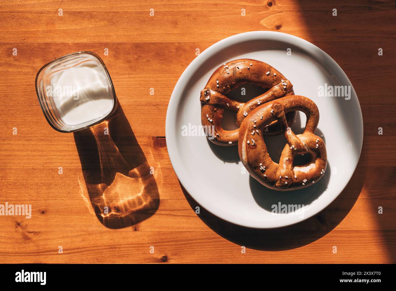 La mattina, due pretzel su un piatto e un bicchiere di yogurt sul tavolo sono perfetti per la colazione, vista dall'alto Foto Stock