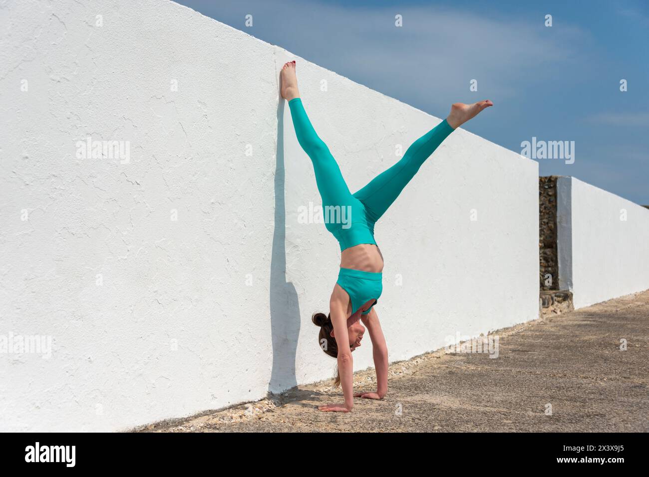 donna che fa una mano accanto a un muro bianco con spazio per le copie. Donna sportiva e sottile che pratica la posa in equilibrio. Foto Stock