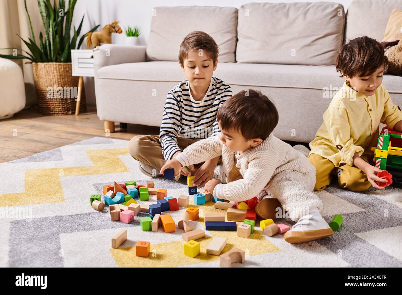 Tre bambini di origine asiatica giocano insieme sul pavimento, impilando blocchi di legno in un soggiorno di casa. Foto Stock