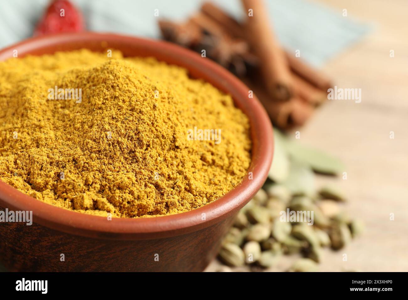 Curry in polvere nel recipiente e altre spezie su tavola di legno, primo piano. Spazio per il testo Foto Stock