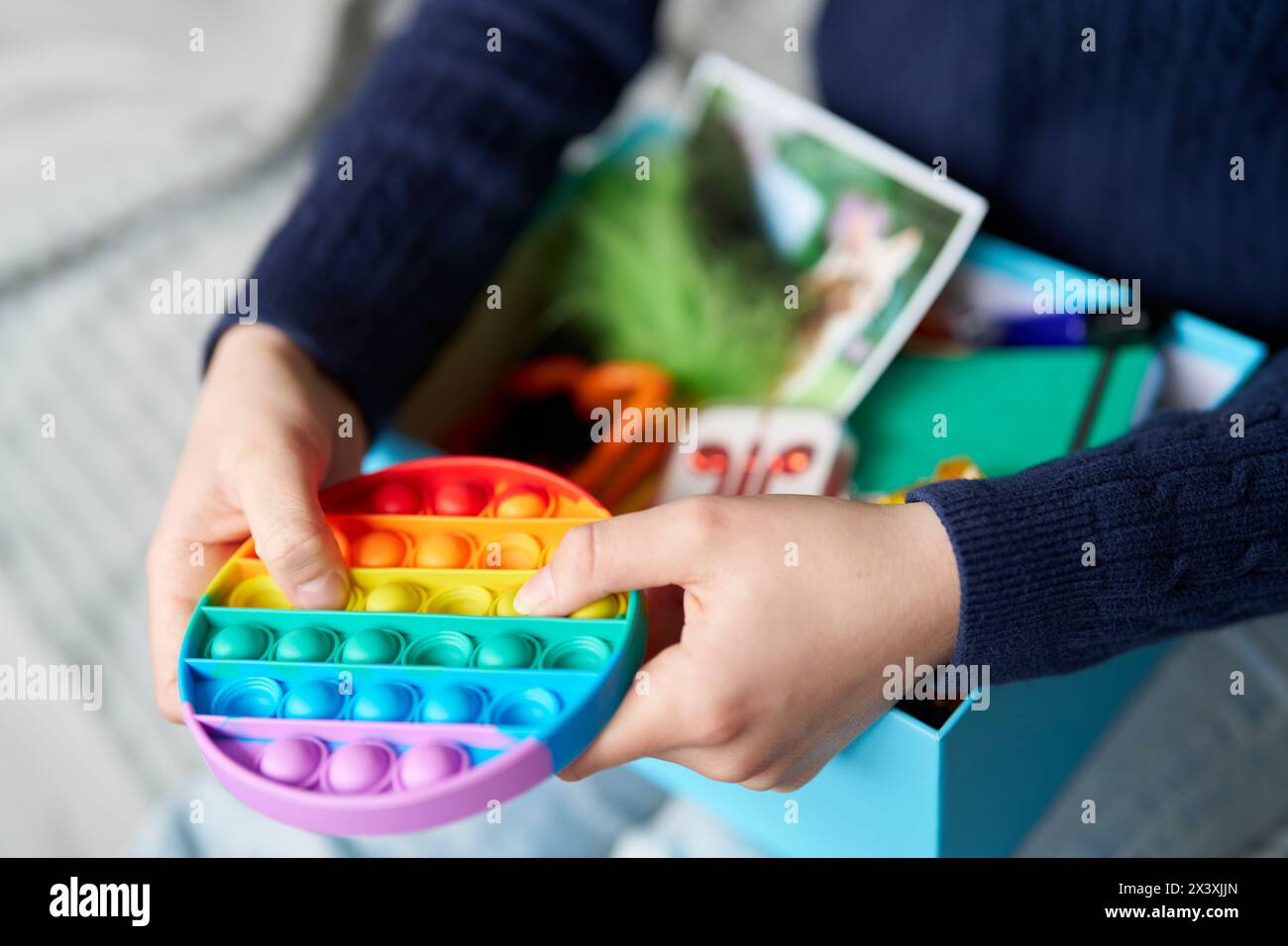 Primo piano di una ragazza adolescente seduta sul letto di casa usando la scatola rilassante contenente foto di animali domestici, Fidget Toy, caramelle o dolci, auricolari per musica, tessuti e SC Foto Stock