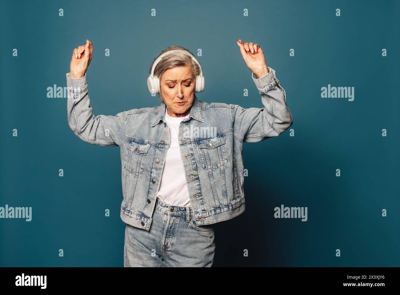 Donna anziana che danzava su uno sfondo blu. Alza le braccia e si muove al ritmo della musica che sta ascoltando con le cuffie. Il suo elegante de Foto Stock