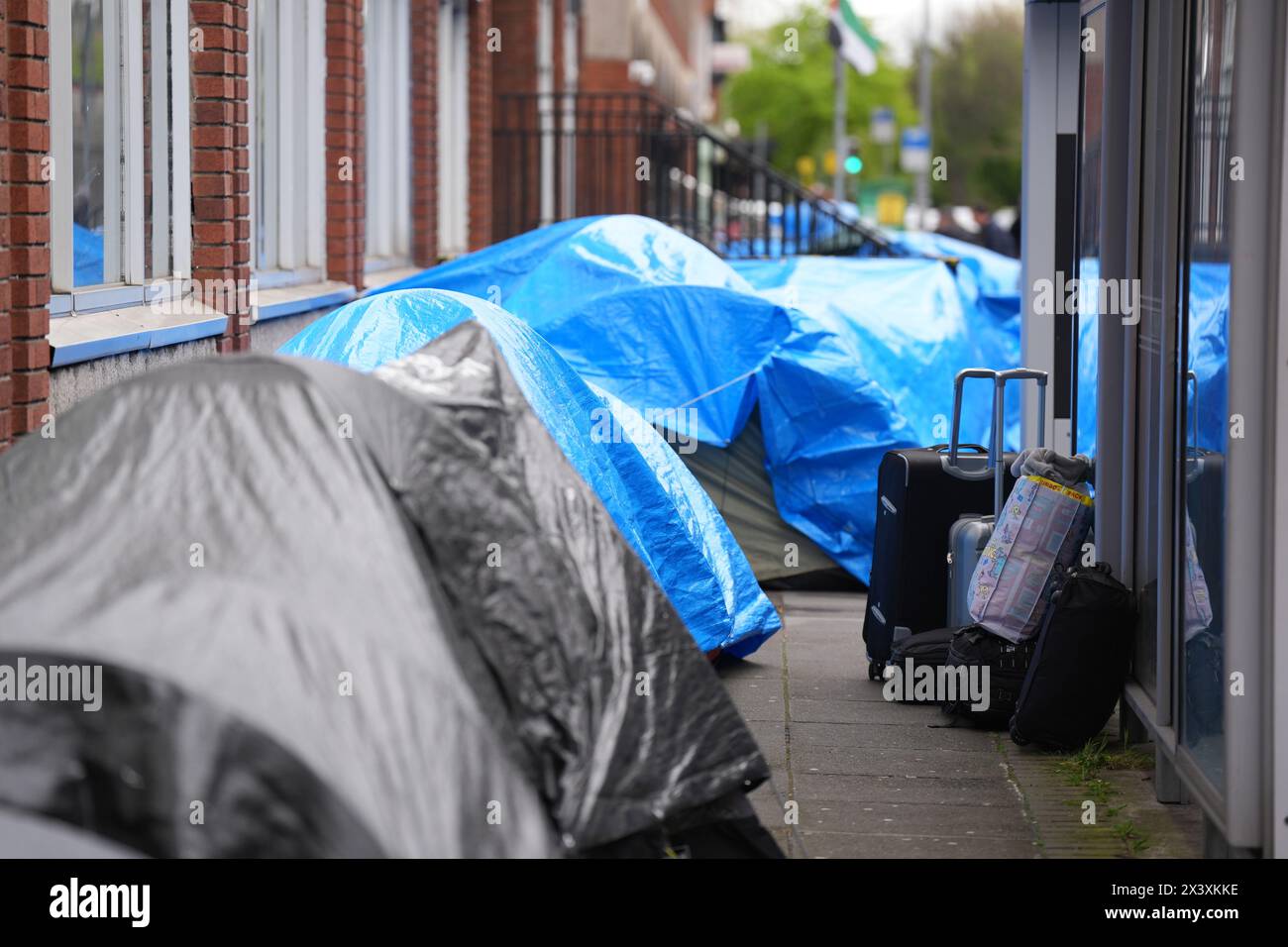 Persone che passano accanto alle tende che ospitano richiedenti asilo vicino all'Ufficio di protezione internazionale, a Dublino. Le affermazioni secondo cui la maggior parte dei richiedenti asilo che entrano in Irlanda aveva attraversato il confine dall'Irlanda del Nord sono state messe in discussione dalle organizzazioni per i diritti umani e i rifugiati. La scorsa settimana, il ministro della giustizia irlandese Helen McEntee ha affermato che il numero di richiedenti asilo che attraversano l'Irlanda del Nord verso lo Stato è ora "superiore al 80 per cento” a seguito di un cambiamento dei modelli migratori negli ultimi mesi. Data foto: Lunedì 29 aprile 2024. Foto Stock