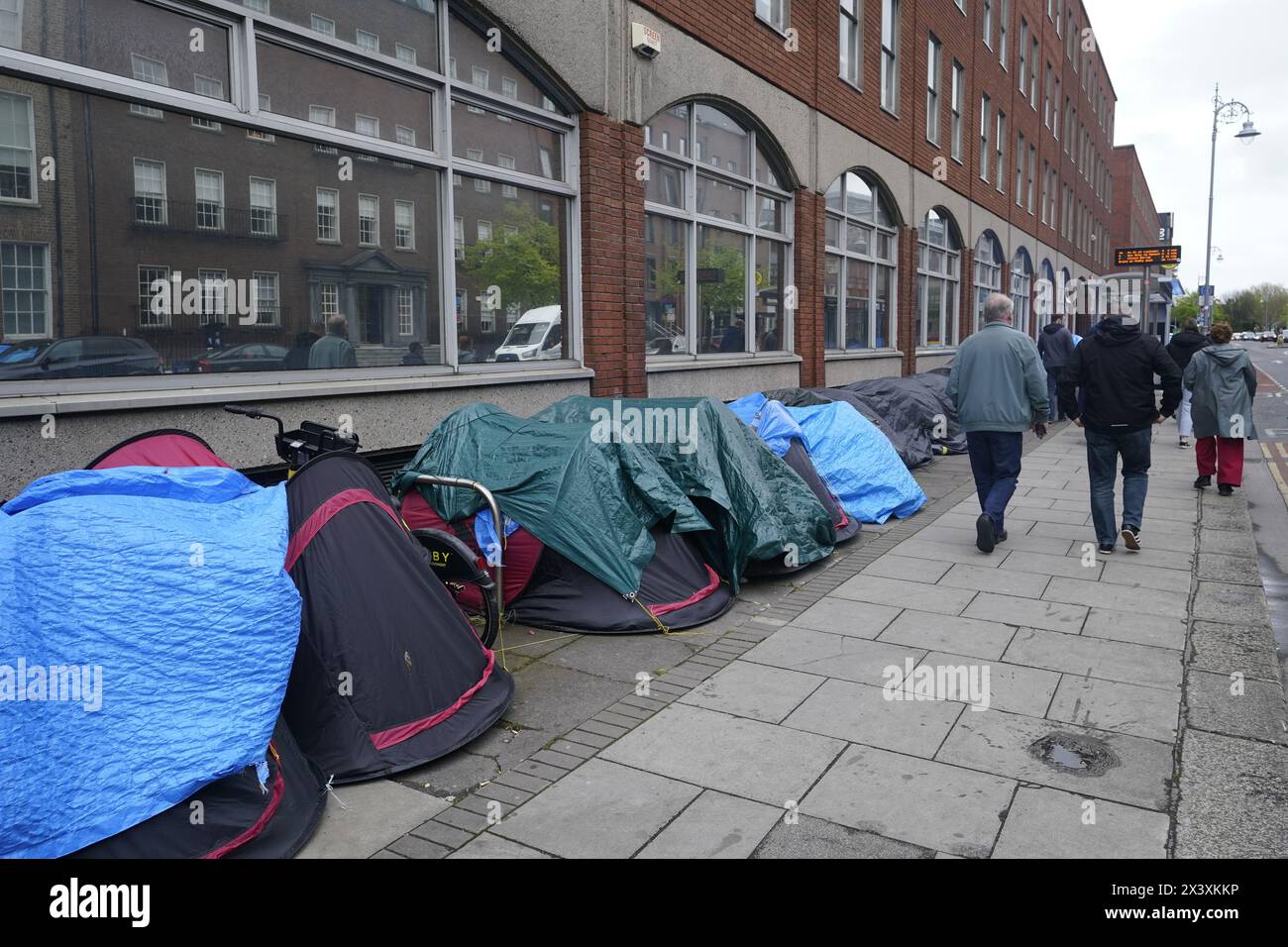 Persone che passano accanto alle tende che ospitano richiedenti asilo vicino all'Ufficio di protezione internazionale, a Dublino. Le affermazioni secondo cui la maggior parte dei richiedenti asilo che entrano in Irlanda aveva attraversato il confine dall'Irlanda del Nord sono state messe in discussione dalle organizzazioni per i diritti umani e i rifugiati. La scorsa settimana, il ministro della giustizia irlandese Helen McEntee ha affermato che il numero di richiedenti asilo che attraversano l'Irlanda del Nord verso lo Stato è ora "superiore al 80 per cento” a seguito di un cambiamento dei modelli migratori negli ultimi mesi. Data foto: Lunedì 29 aprile 2024. Foto Stock