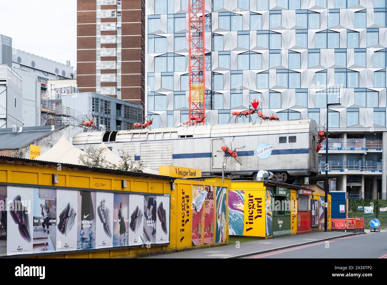 Fotografia di 'Aceto', con una vecchia carrozza del treno sopra bassi edifici dall'aspetto temporaneo, con grandi sculture di formiche rosse posizionate come se strisciassero Foto Stock
