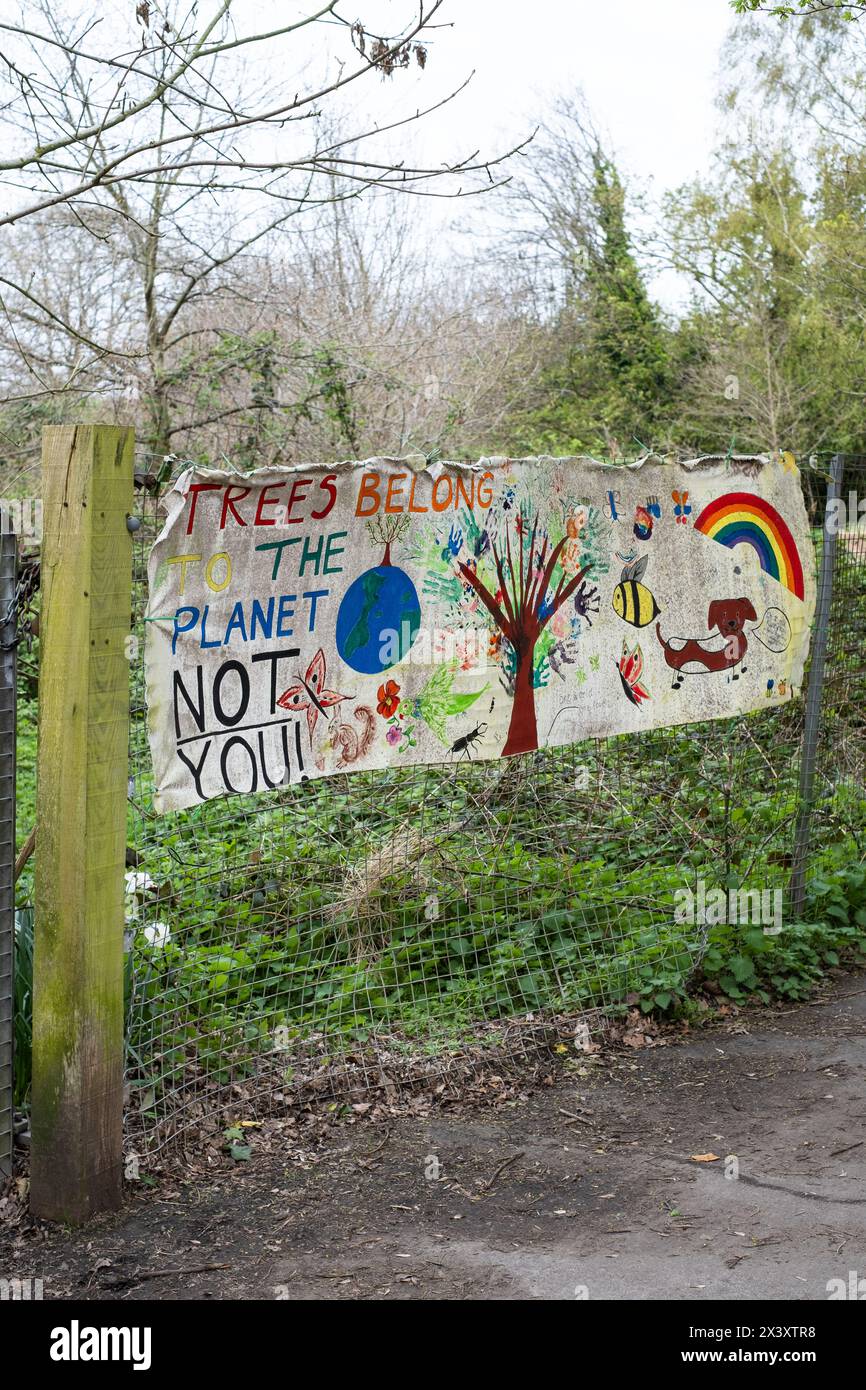 Fotografia di una recinzione metallica con un cartello fatto a mano che dice "gli alberi appartengono al pianeta, non a te" con dipinti per bambini di un albero, il pianeta, un'ape, un Foto Stock
