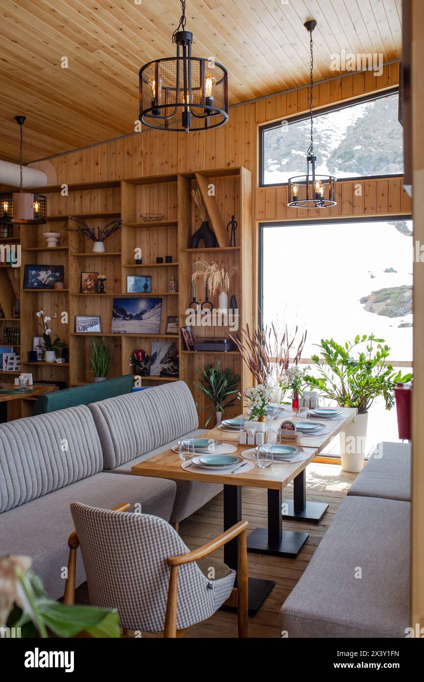 Ristorante rustico con pannelli in legno, grandi finestre, vista sul paesaggio innevato, tavoli, sedie, caminetto e bar che creano un'atmosfera calda. Foto Stock