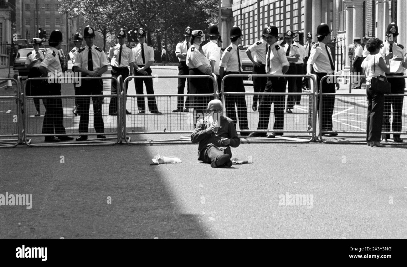 Londra, Regno Unito. 9 giugno 1984. Un solitario attivista non violento e diretto siede di fronte a una linea di polizia vicino all'ingresso di Grosvenor Square, Londra, 9 giugno 1984. L'azione fu in risposta alla visita del presidente americano Ronald Reagan al World Economic Summit di Londra e allo spiegamento dei missili da crociera statunitensi nel Regno Unito. La protesta ha coinciso con il raduno anticrociera del CND a Trafalgar Square. Londra. Grosvenor Square era la sede dell'ambasciata americana nel Regno Unito al momento della protesta. Foto Stock