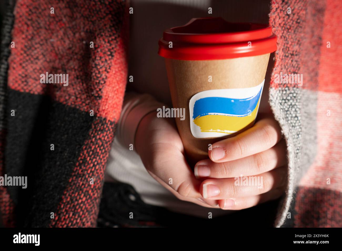 Tazza di caffè in cartone con un adesivo a forma di bandiera nazionale dell'Ucraina in primo piano. Blackout. Interruzioni di corrente Foto Stock