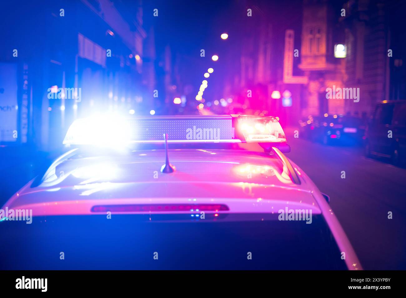 UN'AUTO DELLA POLIZIA È IN PIEDI SULLA SCENA DELL'INCIDENTE IN CITTÀ CON LE SIRENE E I LAMPEGGIANTI ACCESI. Vecchie case sfocate sullo sfondo. Foto Stock