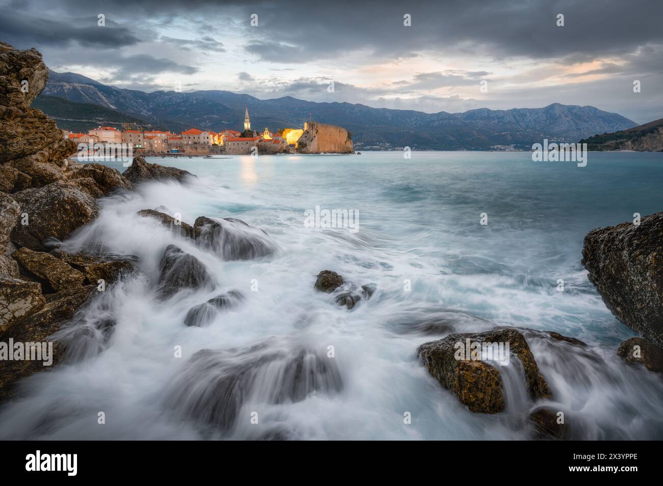 Tramonto tempestoso sulle antiche rocce costiere di Budva e le onde che si infrangono Foto Stock