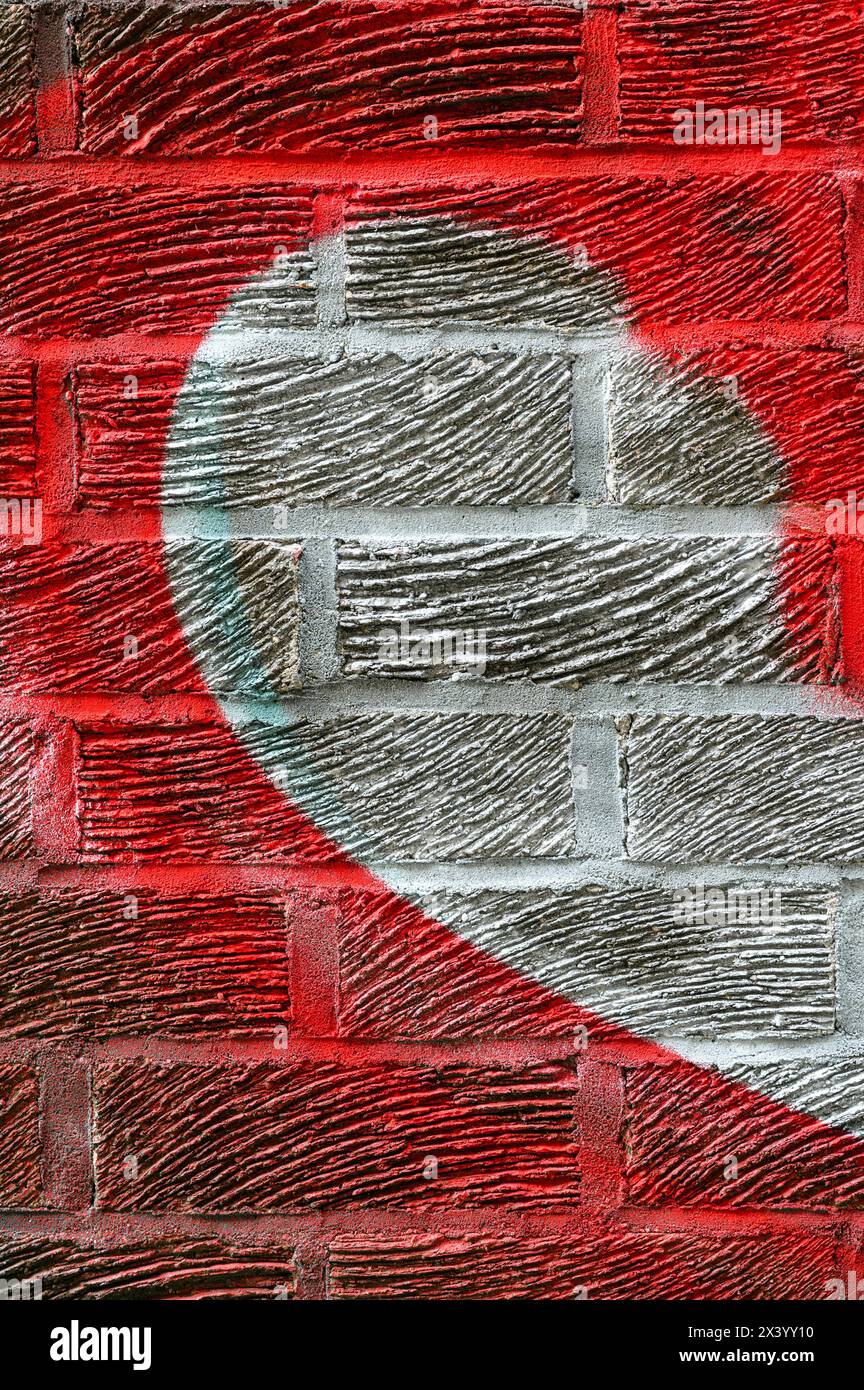 Metà di uno spray a forma di cuore dipinto in rosso e bianco su una parete di mattoni Foto Stock
