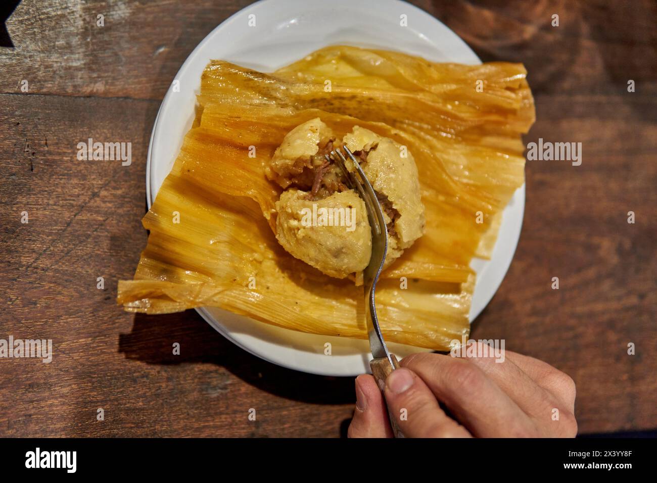 la mano di un uomo che divide un tamale con una forchetta. cibo tipico argentino, impasto di farina di mais ripieno di manzo, maiale o a strappo, oltre ad altri ingredienti gustosi. Foto Stock