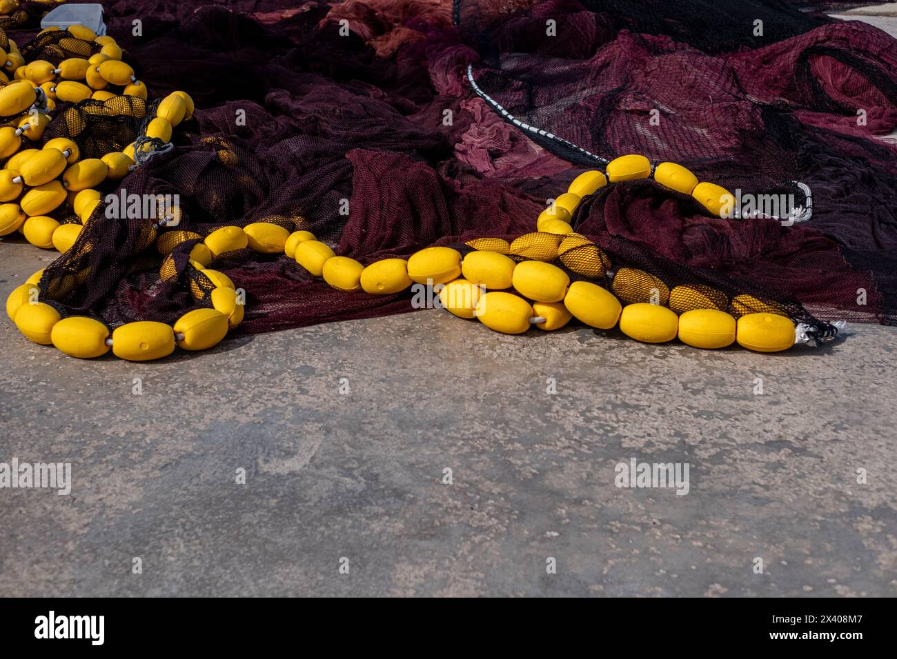 Un primo piano di attrezzature da pesca, dove i galleggianti di colore giallo brillante contrastano con la maglia scura delle reti, pronte per la raccolta dei mari. Foto di alta qualità Foto Stock