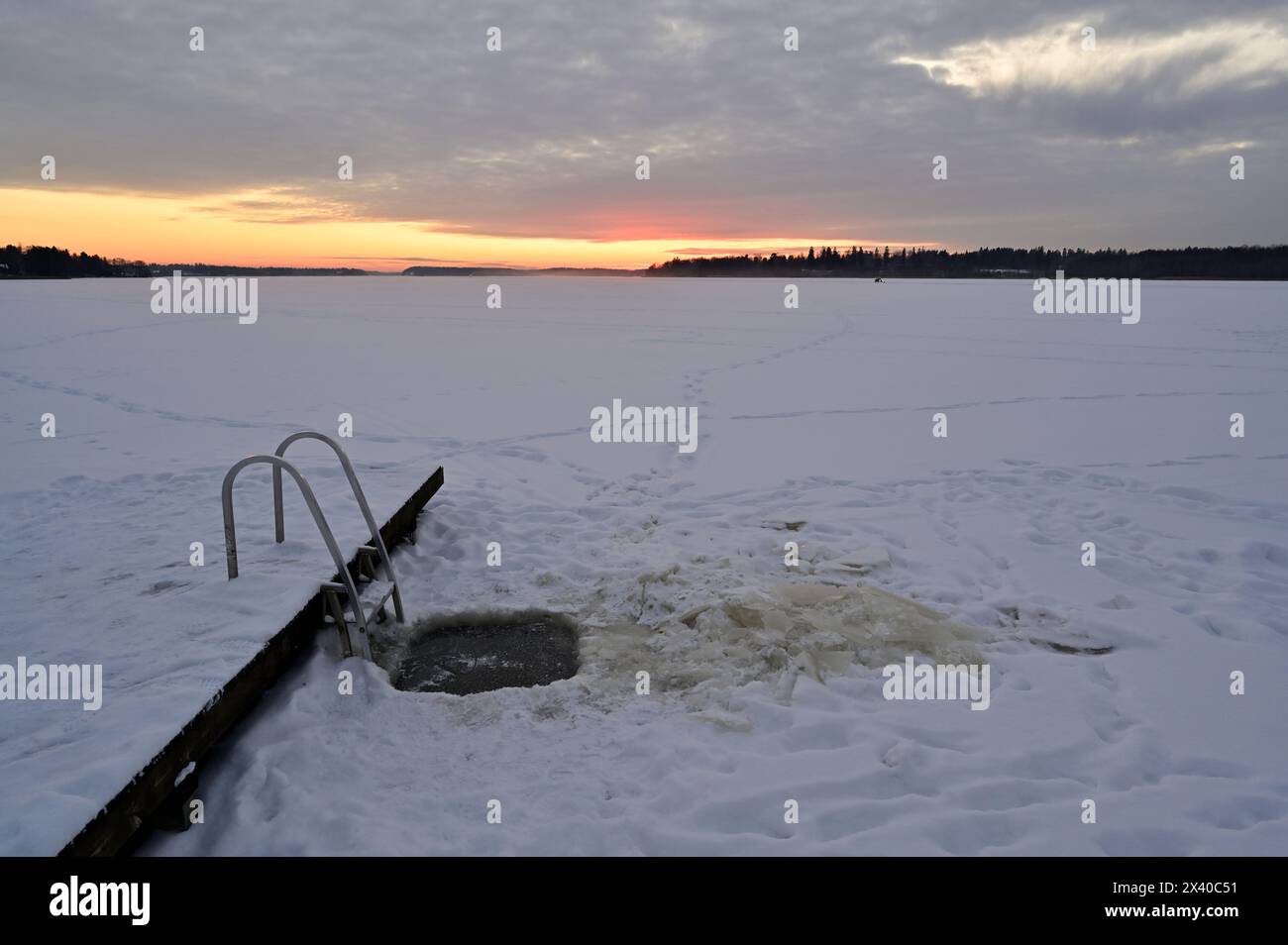 Contro il paesaggio ghiacciato, una scala solitaria si erge alta, raggiungendo il tramonto infuocato, mentre il freddo cielo invernale e le nuvole abbracciano la quiete di Foto Stock
