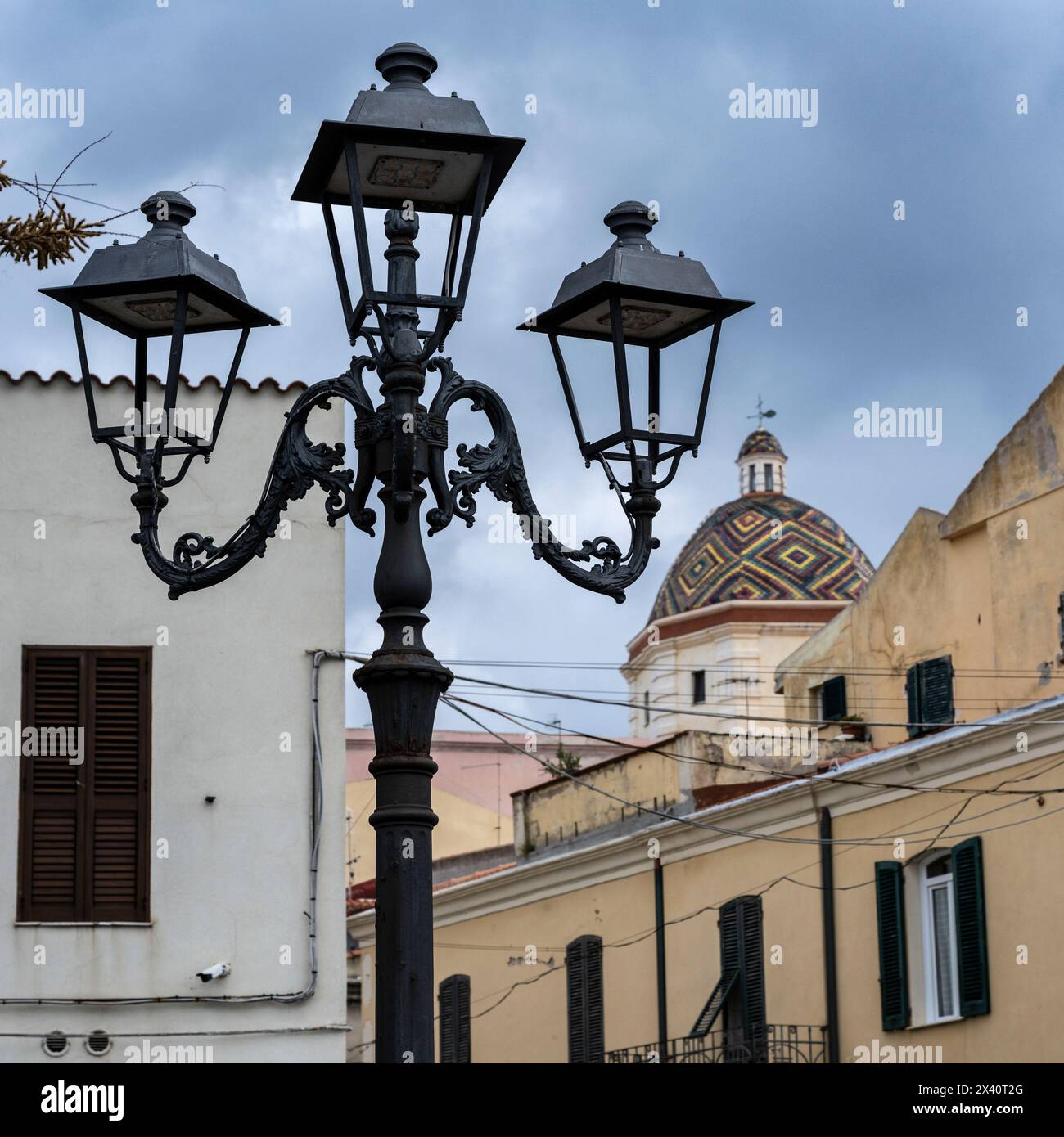 Primo piano di uno standard di luce decorativa in metallo nero e della cupola colorata della Chiesa di San Michele ad Alghero, Italia. Alghero è una città sulla T... Foto Stock