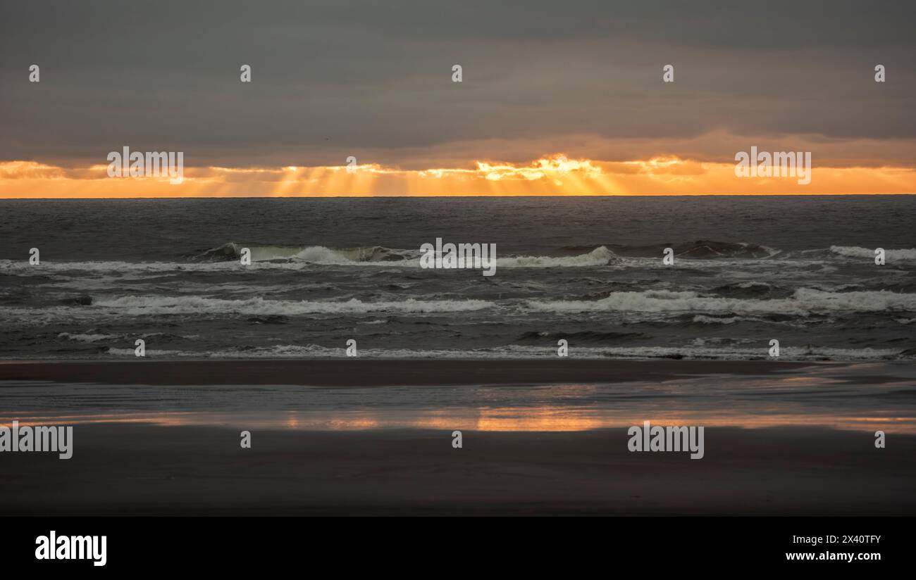 Splendido tramonto con le dita di Dio che si estendono da dietro le nuvole sull'Oceano Pacifico dalla spiaggia del Cape Disappointment State Park ... Foto Stock