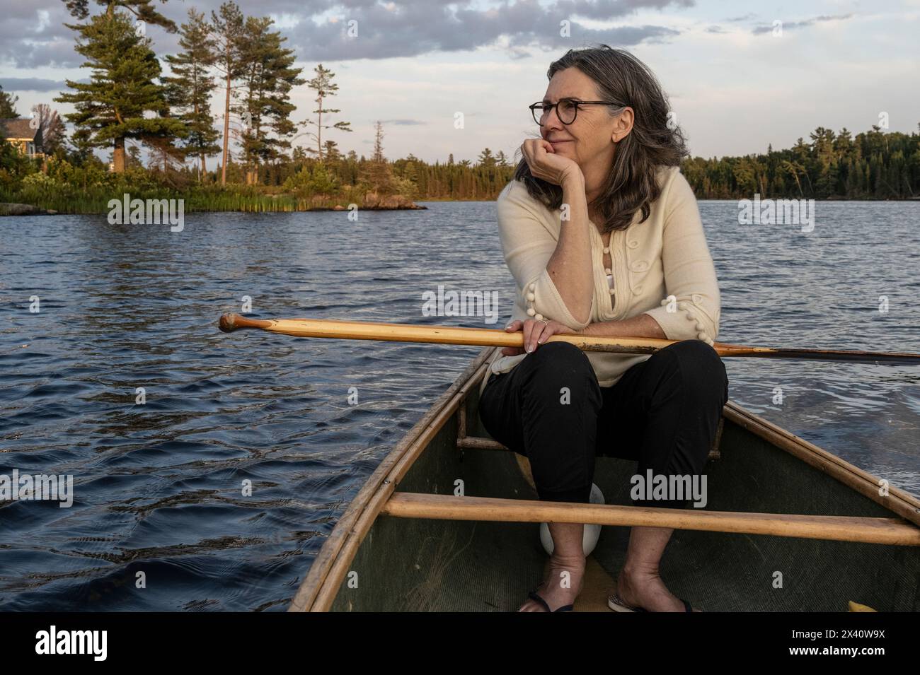 La donna si rilassa in una canoa galleggiante mentre guarda la bellezza naturale lungo la costa del lago; Lake of the Woods, Ontario, Canada Foto Stock