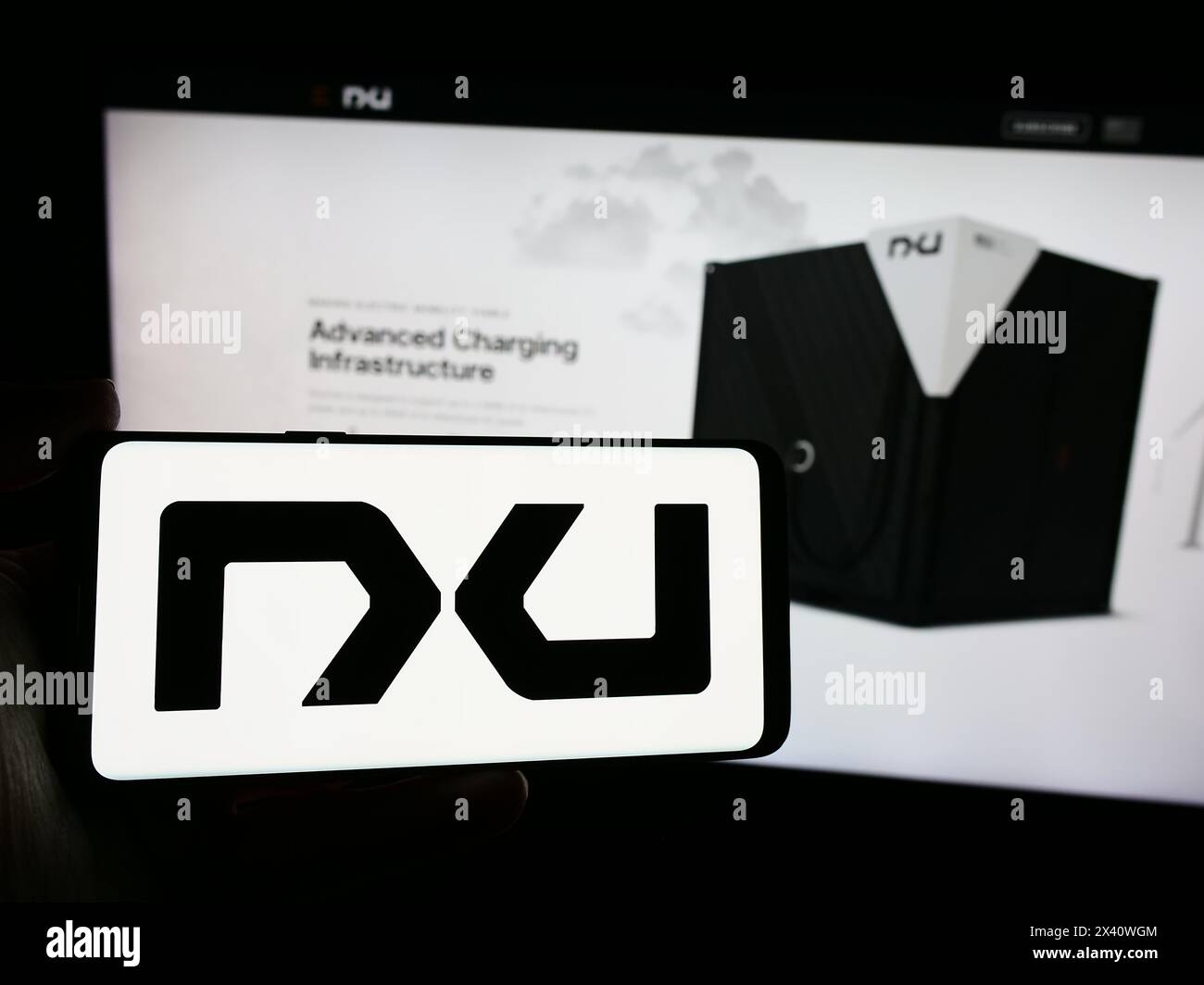Persona che possiede uno smartphone con il logo dell'azienda statunitense Nxu Inc. Di fronte al sito Web. Mettere a fuoco il display del telefono. Foto Stock