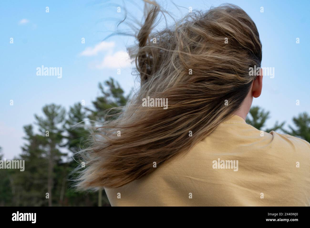 La ragazza sta fuori con la maglietta e i capelli lunghi che soffiano al vento; Lake of the Woods, Ontario, Canada Foto Stock