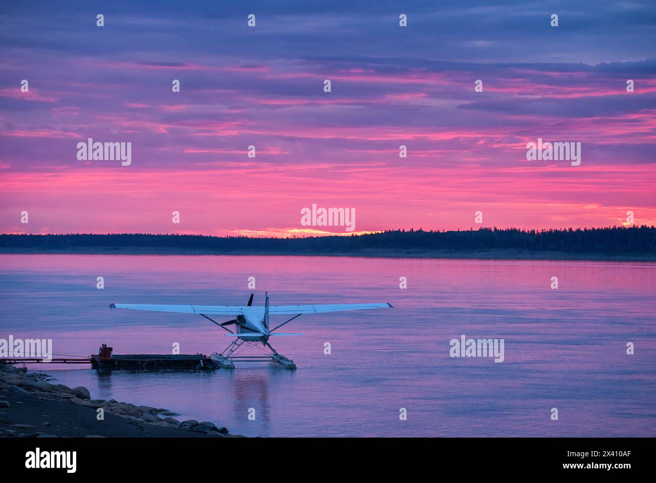 Idrovolante nel fiume Mackenzie mentre il sole tramonta illumina le nuvole in splendidi rosa; Fort Simpson, territori del Nord-Ovest, Canada Foto Stock