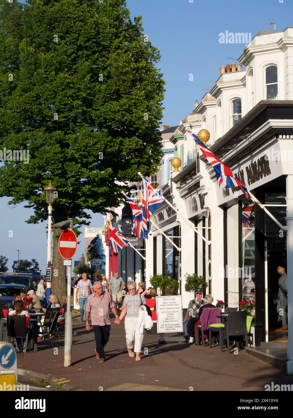 Persone sedute ai tavoli all'esterno e passeggiate su Carlisle Road con Union Jacks Flying, Eastbourne, East Sussex, Regno Unito; Eastbourne, East Sussex, Inghilterra Foto Stock