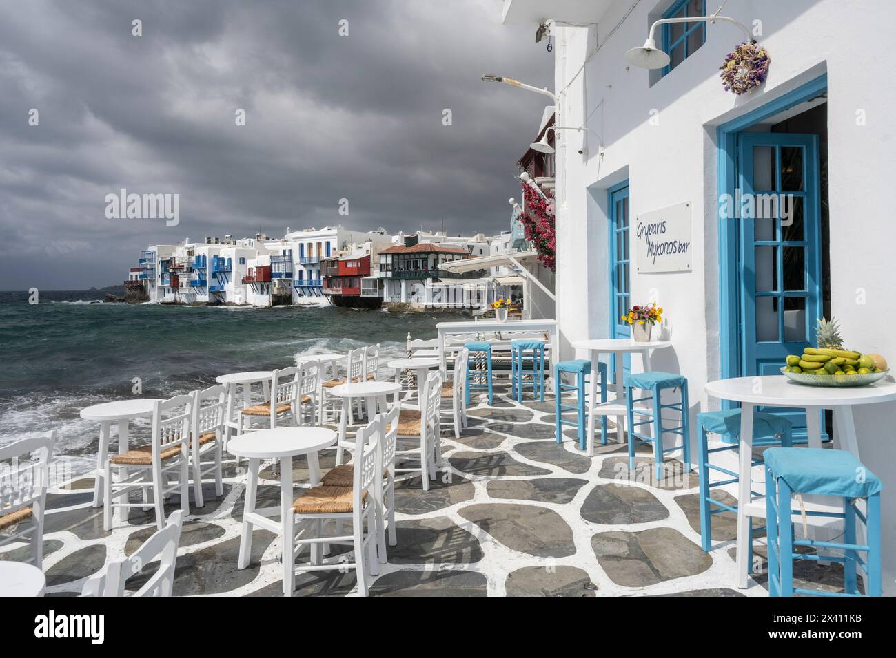 Posti a sedere su un patio esterno sul lungomare dell'isola di Mykonos, con vista sulle case dei pescatori di Little Venice; Mykonos, Grecia Foto Stock