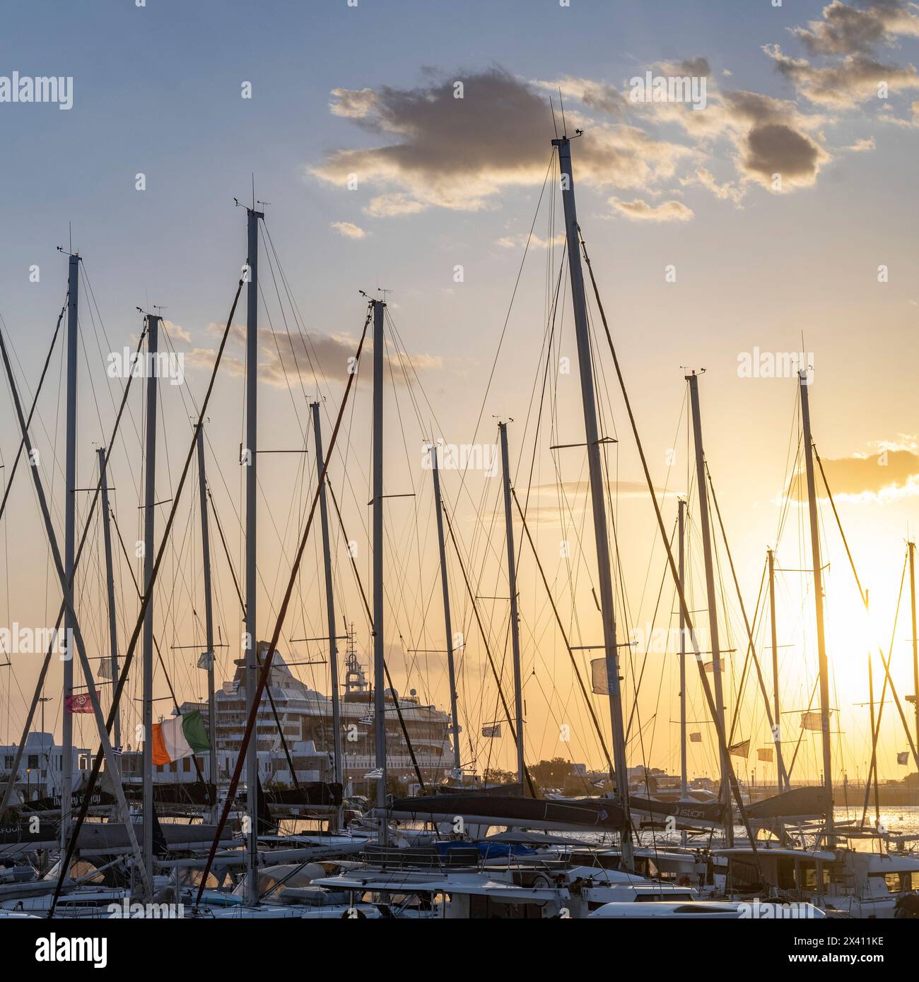 Nave da crociera nel porto di Mykonos con un sole luminoso al tramonto e barche a vela nel porto in primo piano; Mykonos, Egeo meridionale, Grecia Foto Stock