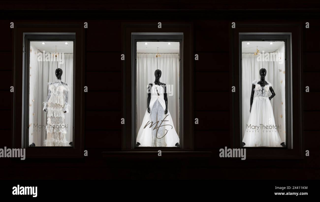 Abiti da sposa bianchi lunghi sul pavimento, in mostra su manichini dalla pelle scura in vetrine illuminate di notte Foto Stock