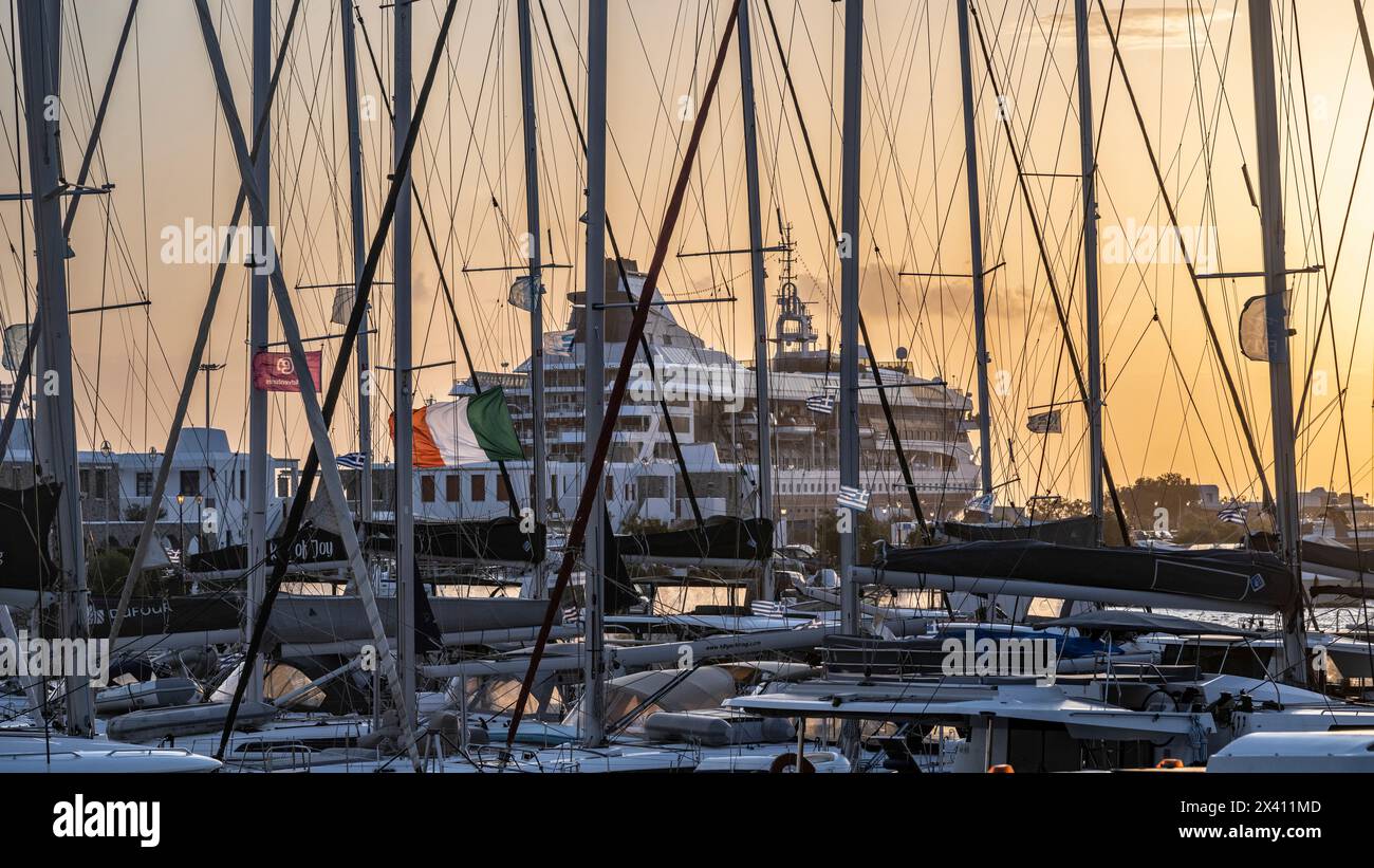 Crociera nel porto di Mykonos con un cielo dorato scintillante al tramonto e barche a vela nel porto in primo piano; Mykonos, Egeo meridionale, Grecia Foto Stock